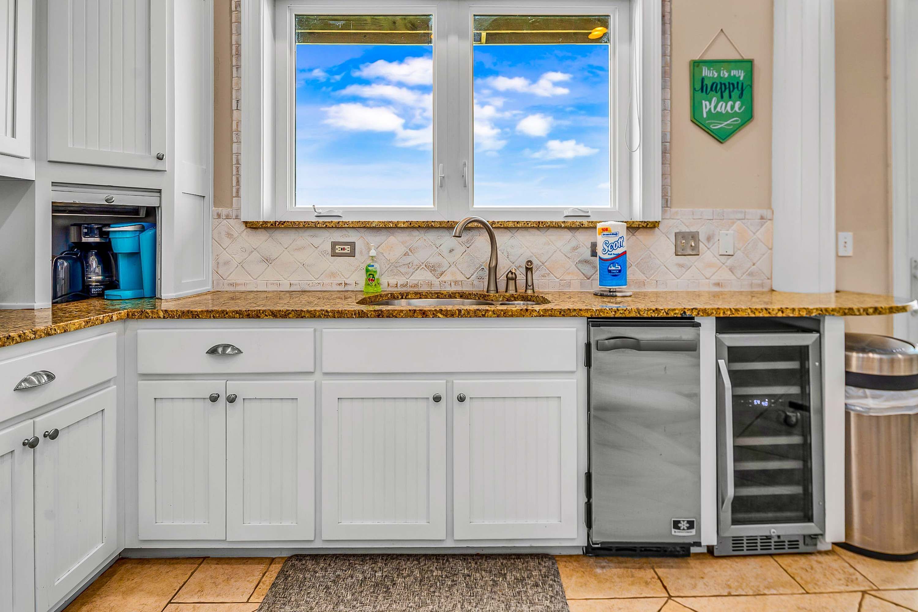 A kitchen with white cabinets, a granite countertop, a stainless steel sink, and a dishwashing machine.