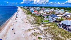 A coastal residential area with beachfront properties, a sandy beach, and a clear blue sky. - Gulf-front home with direct beach access, Gulf views, yard, & deck (St. George Island)