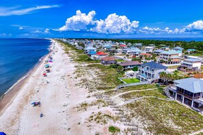 A coastal residential area with beachfront properties, a sandy beach, and a clear blue sky. - Gulf-front home with direct beach access, Gulf views, yard, & deck (St. George Island)