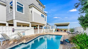 A swimming pool with lounge chairs, a covered patio, and a two-story building with a white fence. - Gulf-front home with direct beach access, Gulf views, yard, & deck (St. George Island)