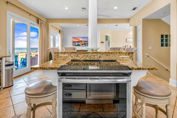 A kitchen with a granite countertop, a built-in oven, and two bar stools. - Gulf-front home with direct beach access, Gulf views, yard, & deck (St. George Island)
