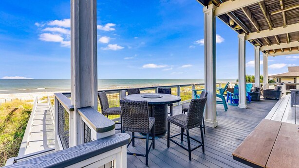 A covered outdoor deck with a round table and chairs, overlooking a beach. - Gulf-front home with direct beach access, Gulf views, yard, & deck (St. George Island)