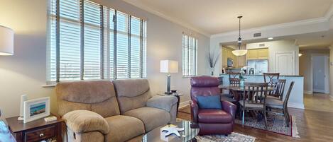 A living room with a sofa, armchair, and coffee table, a dining area with a table and chairs, and a kitchen in the background.