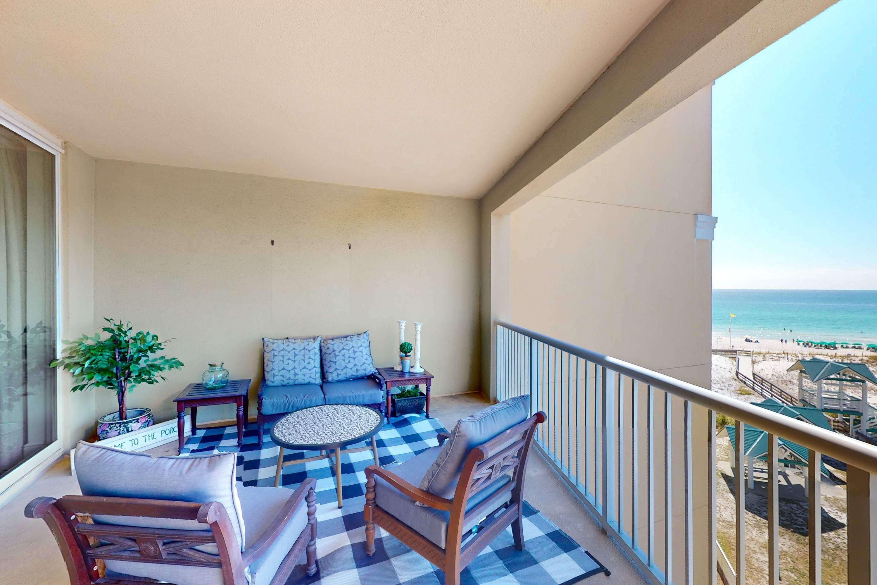 Ein Balkon mit kariertem Boden, einer Couch, zwei Stühlen, einem kleinen Tisch und einem Blumentopf.