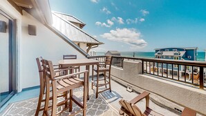 A balcony with wooden furniture, a view of the sea, and a building in the background. - Renovated oceanfront condo with lanai, pool, hot tub & view - snowbird-friendly (Mexico Beach)