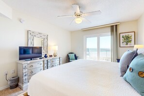 A hotel room with a large bed, a ceiling fan, a television, a dresser, and a window with a view. - Gulf-front condo with balcony, ocean view, W&D, pool, & fitness room (Fort Walton Beach)