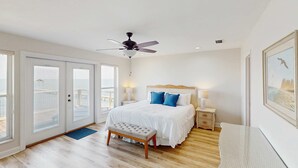 Een slaapkamer met een bed, een plafondventilator, een bankje en uitzicht door de schuifdeuren.