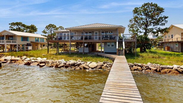 Een pand aan het water met een houten steiger naar een huis met meerdere balkons en een overdekt terras.