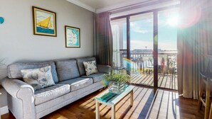 Sala de estar com um sofá cinzento, uma mesa de centro de vidro e vista para uma varanda com guarda-corrimão.
