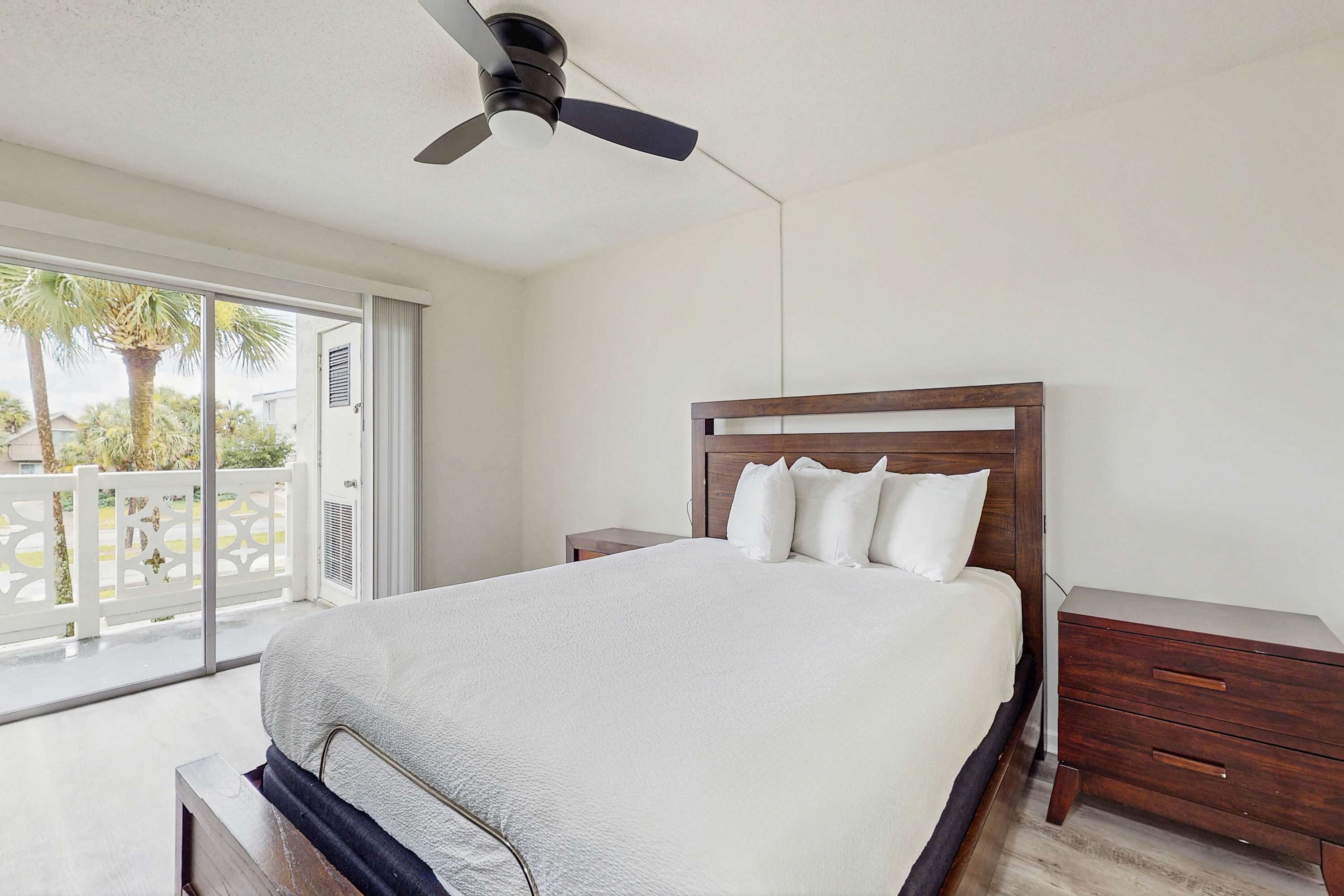 Quarto com cama, mesa de cabeceira, penteadeira de madeira e ventilador de teto.