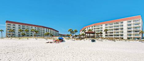 Ein Strandhotel mit mehreren Etagen, Palmen und einem Sandstrand im Vordergrund.