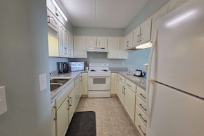 A compact kitchen with white cabinets, a stove, and a refrigerator. - Gulf view condo with private balcony, close to beaches and more! (Fort Walton Beach)