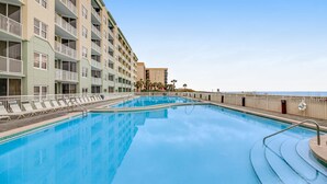 Una piscina al costat d'un hotel de diverses plantes amb balcons, un post de socorristes i una vista despejada de l'oceà.