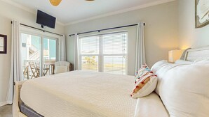 Habitación de hotel con una cama grande, ventilador de techo, televisor montado en la pared y balcón con vistas al exterior.