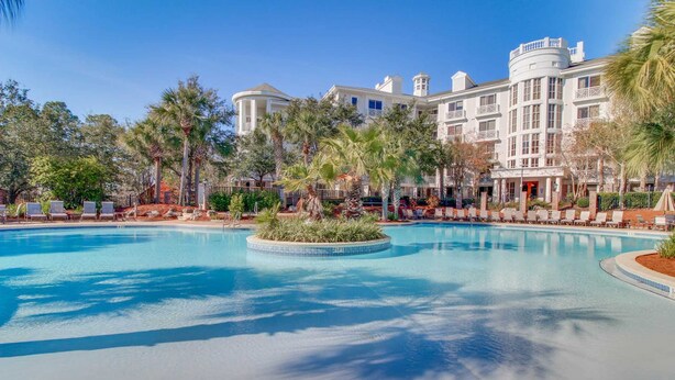 A large pool with lounge chairs and palm trees, surrounded by a building with multiple stories and balconies. - Ideal getaway near the beach & golf with shared pool, central AC (Miramar Beach)