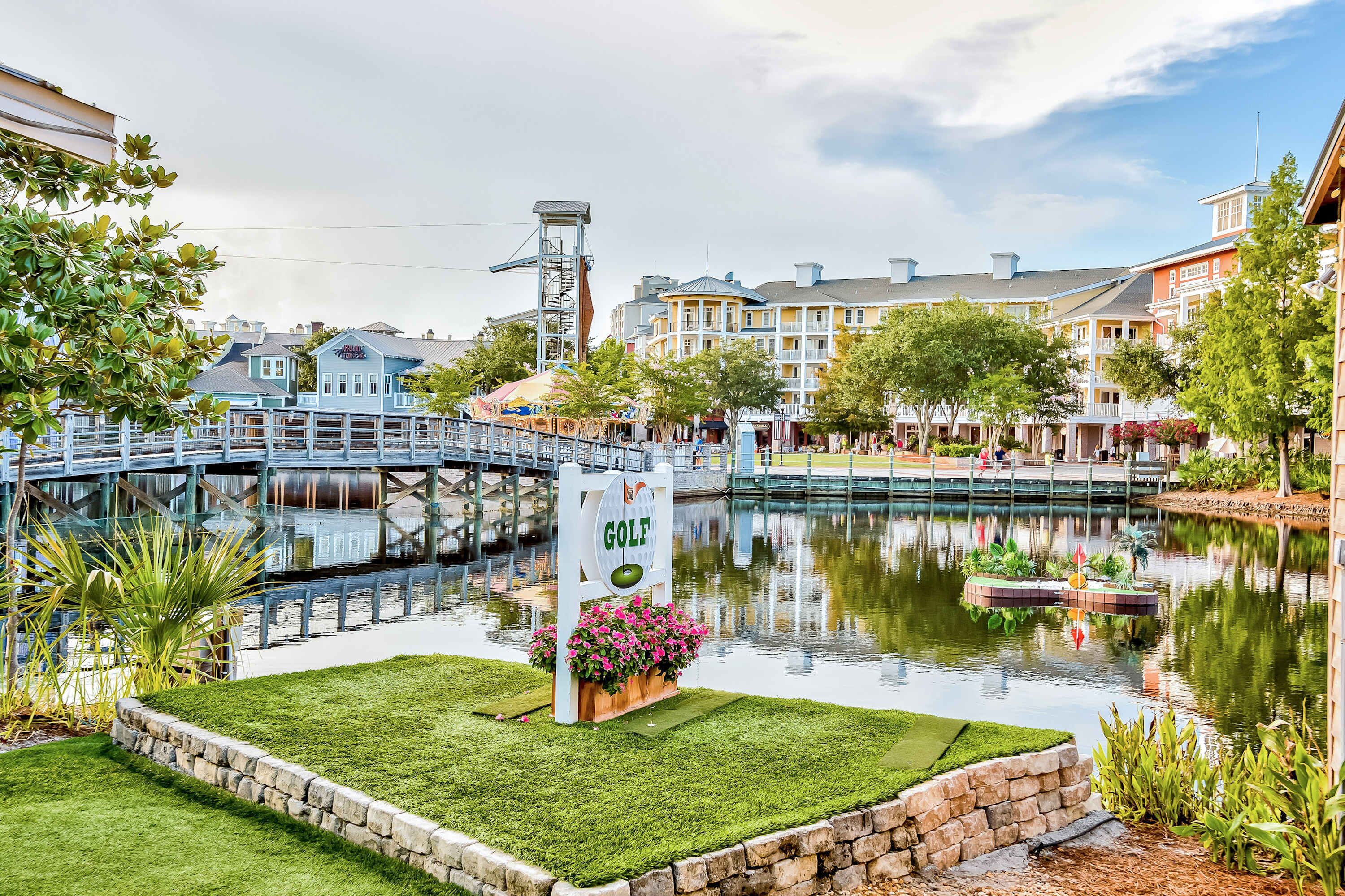 Campo de golf con un letrero, un puente y un reflejo en el agua.