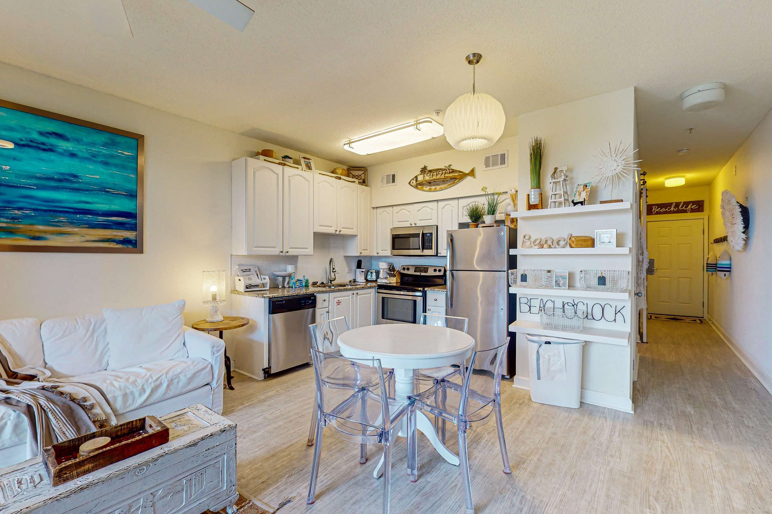 Una cocina moderna con armarios blancos, una zona de comedor con una mesa redonda y sillas, y una sala de estar con un sofá blanco.