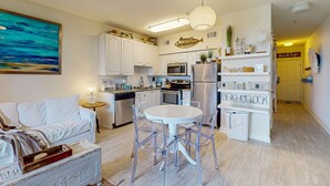 Una cocina moderna con armarios blancos, una zona de comedor con una mesa redonda y sillas, y una sala de estar con un sofá blanco.