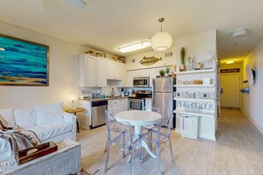 A modern kitchen with white cabinetry, a dining area with a round table and chairs, and a living room with a white sofa. - Adorable 3rd-floor cabana with gorgeous view from balcony, pool and hot tub access (Santa Rosa Beach)