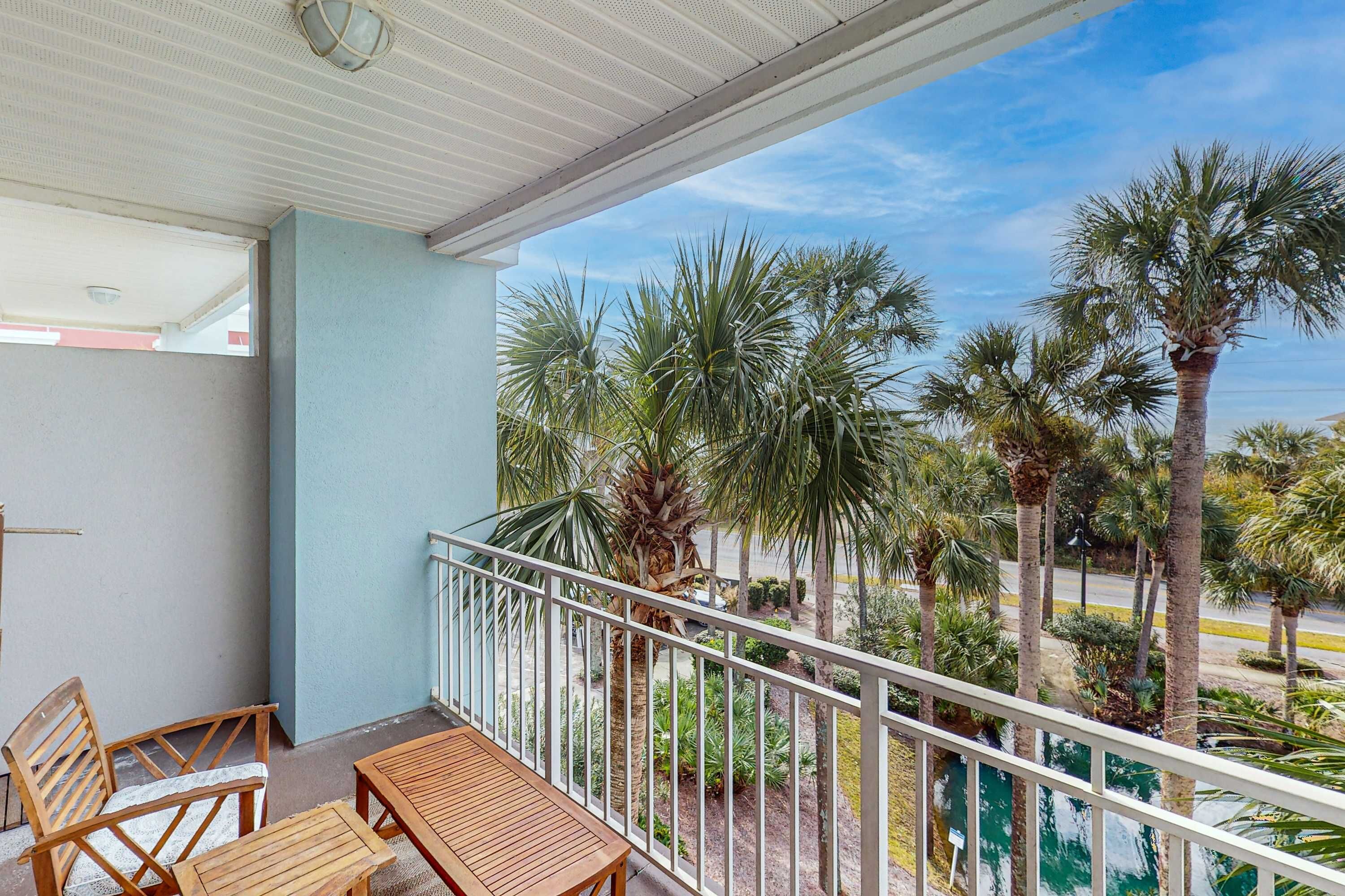 A balcony with wooden furniture, a railing, and a view of palm trees and greenery.