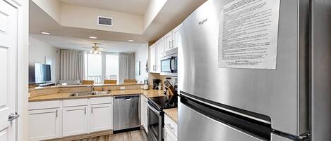 A modern kitchen with stainless steel appliances, white cabinetry, and a wooden floor.