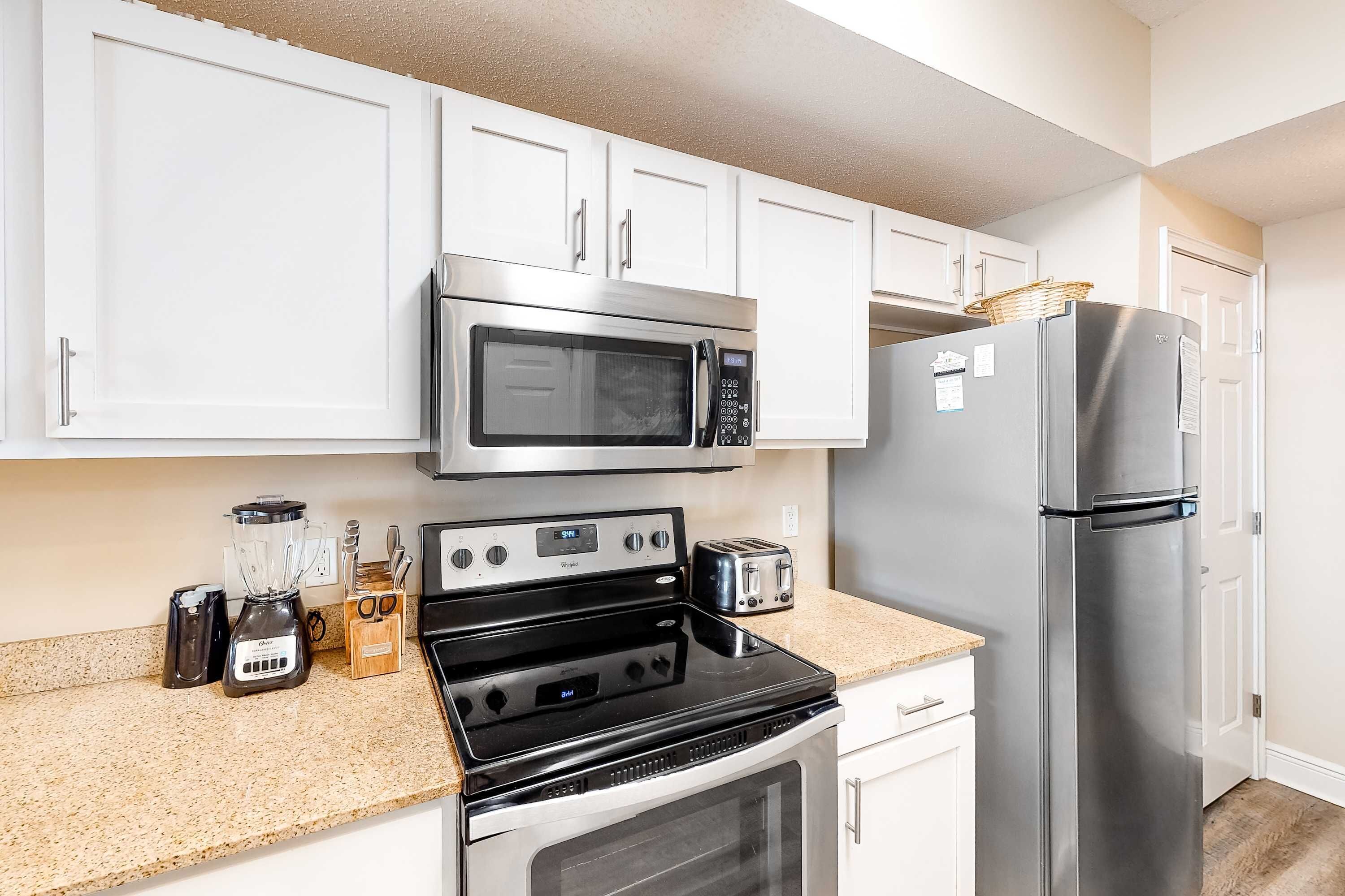 A modern kitchen with white cabinets, stainless steel appliances including a microwave, refrigerator, stove, and toaster.
