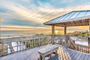 Eine Holzterrasse mit einer Bank, die auf einen Strand mit einem Holzsteg und einem Pavillon blickt.