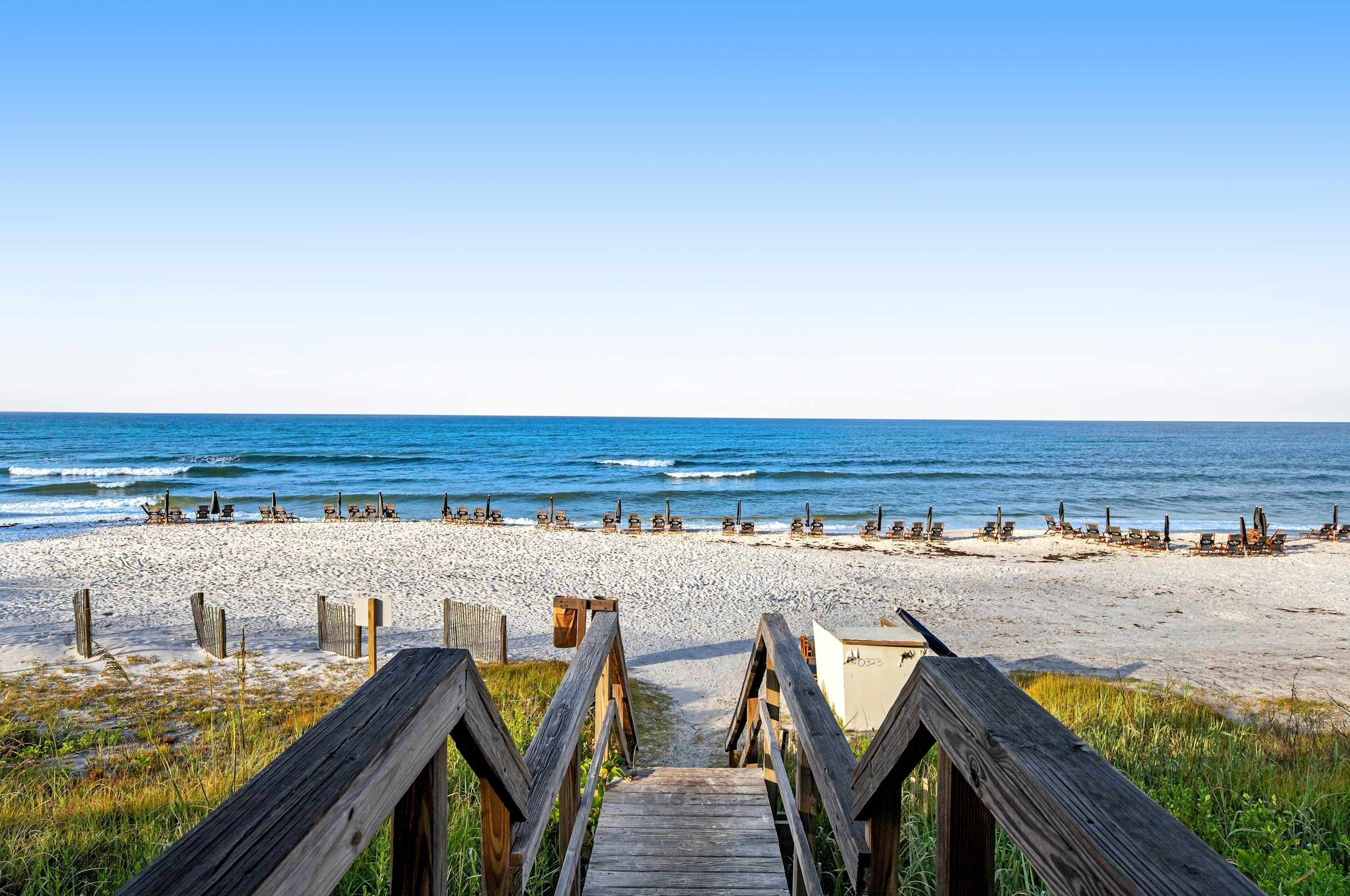 A wooden boardwalk leading to a beach with rows of sun loungers.