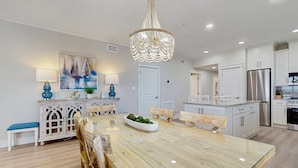 Una cocina moderna con armarios blancos, un refrigerador de acero inoxidable y una zona de comedor con mesa de vidrio y sillas de madera.
