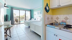 Quarto de hotel com varanda, cozinha compacta e cama.