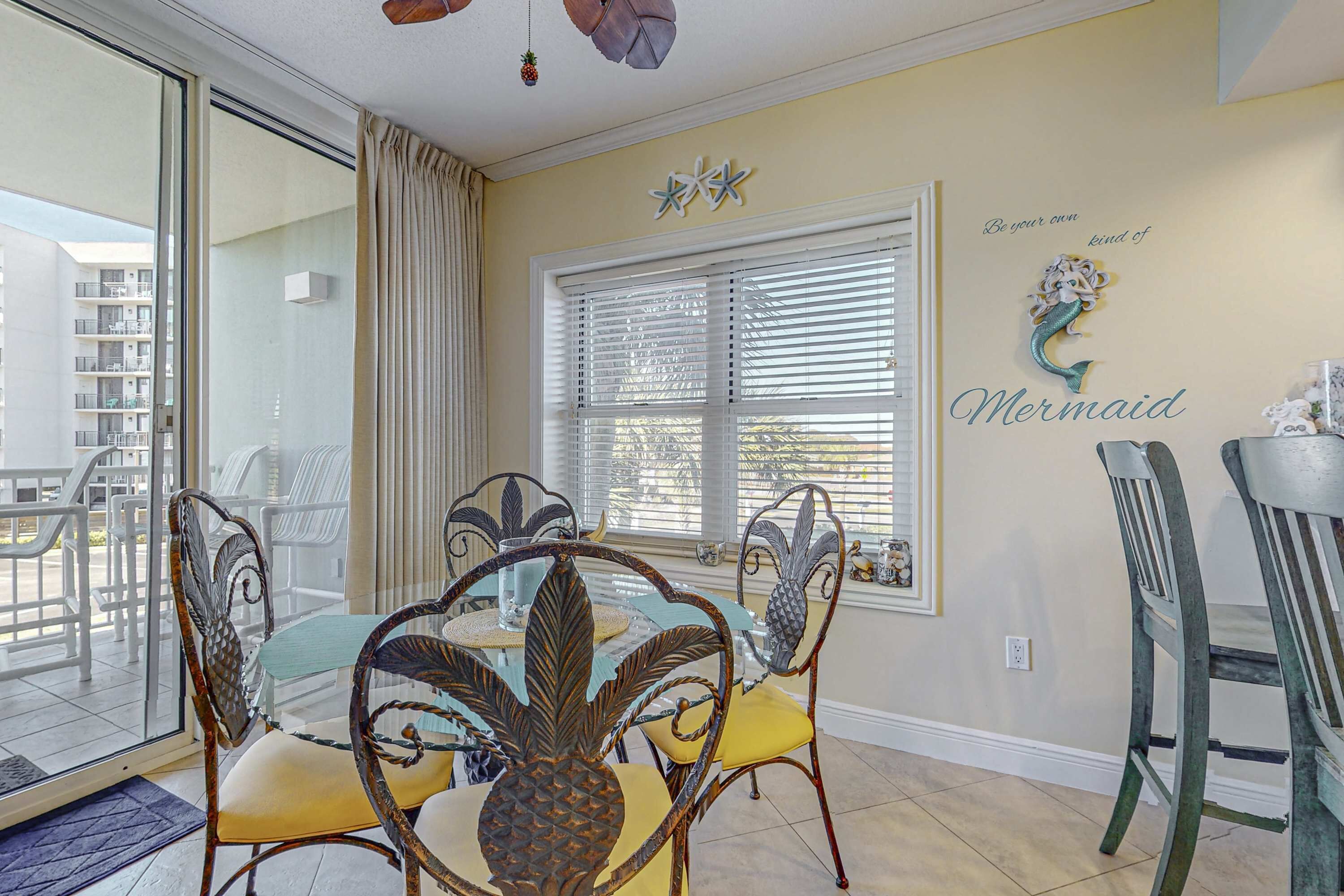 Un coin repas avec une table en verre, des chaises ornées de motifs ananas et une vue sur le balcon extérieur.