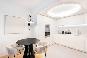 A modern kitchen with white cabinetry, a round dining table with two chairs, and a pendant light. - Bolhão Luxe | High-End Retreat by the Market (Porto)