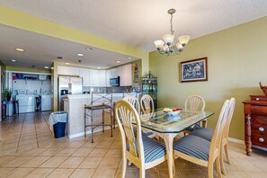 A spacious kitchen with white cabinets, a central island, and a dining area with a glass table and wooden chairs. - Partial Gulf View, Community Pools, Onsite Fitness Center, Free WiFi (Pensacola Beach)