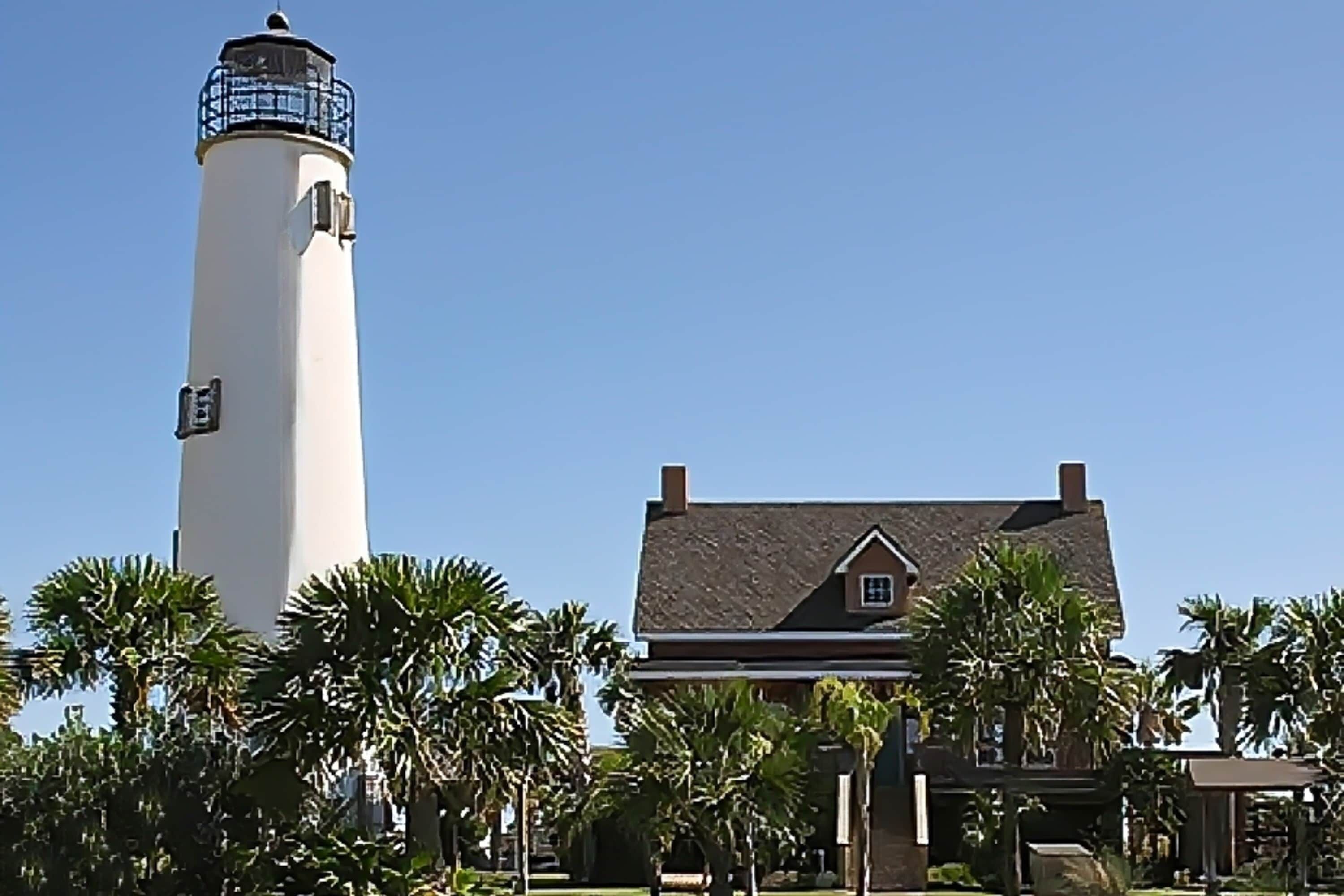 A lighthouse and a house with a gabled roof, surrounded by palm trees.