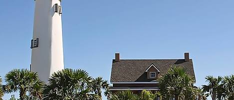 A lighthouse and a house with a gabled roof, surrounded by palm trees.