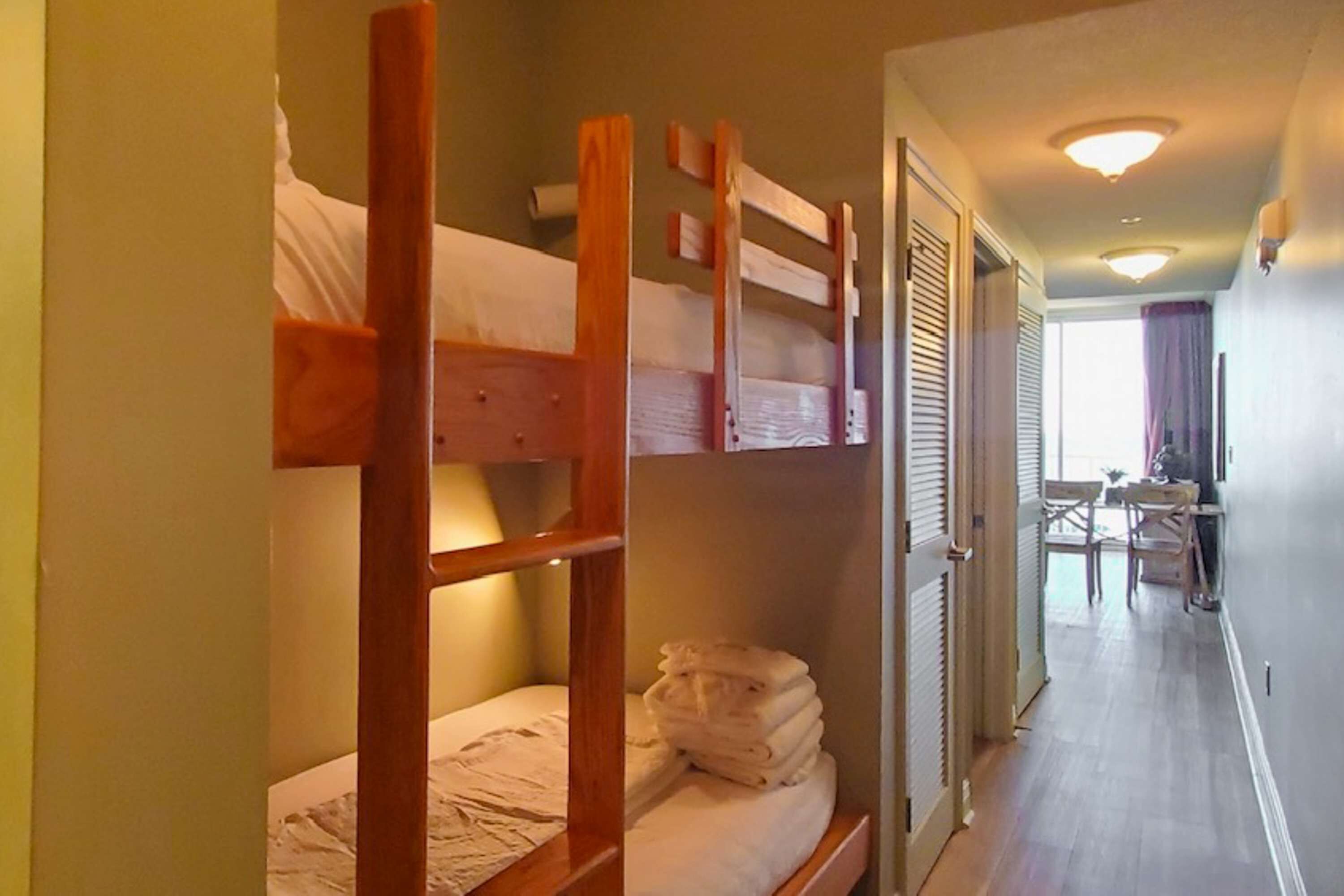 Un letto a castello con struttura in legno e biancheria bianca, un tavolino con sedie e una finestra con tende.