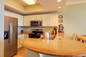 A kitchen with white cabinets, a stainless steel refrigerator, a microwave, a stove, and a sink. - Beachfront 3rd Floor Condo w Private Balcony, Shared Heated Pool, Beach Access (Fort Walton Beach)