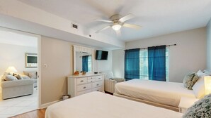 Ein Schlafzimmer mit zwei Betten, einem Deckenventilator, einem Fernseher und einem Fenster mit Vorhängen.