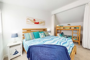 Een slaapkamer met een bed, nachtkastje, stapelbed en een kunstwerk aan de muur.