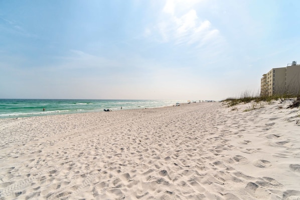 Een zandstrand met voetafdrukken, een gebouw aan de rechterkant en de oceaan op de achtergrond.