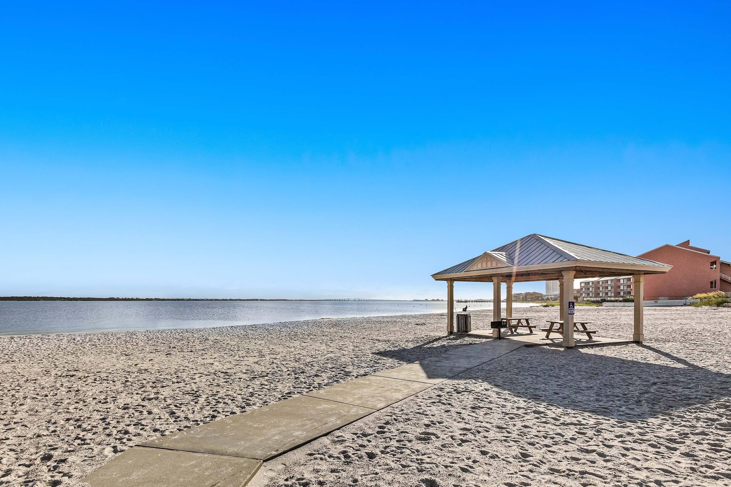 Uma praia com um pavilhão coberto, mesas de piquenique e vista clara para o mar.