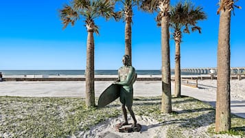 A statue of a person holding a surfboard, surrounded by palm trees and a clear blue sky.