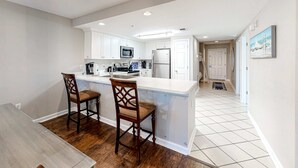 Une cuisine moderne avec des meubles blancs, un îlot central et deux tabourets de bar en bois.