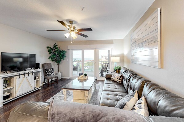 A living room with a TV, sofa, coffee table, and ceiling fan. - 3rd Floor Condo with Shared Pools,Tennis, Private W&D, WiFi, and Central AC (Miramar Beach)