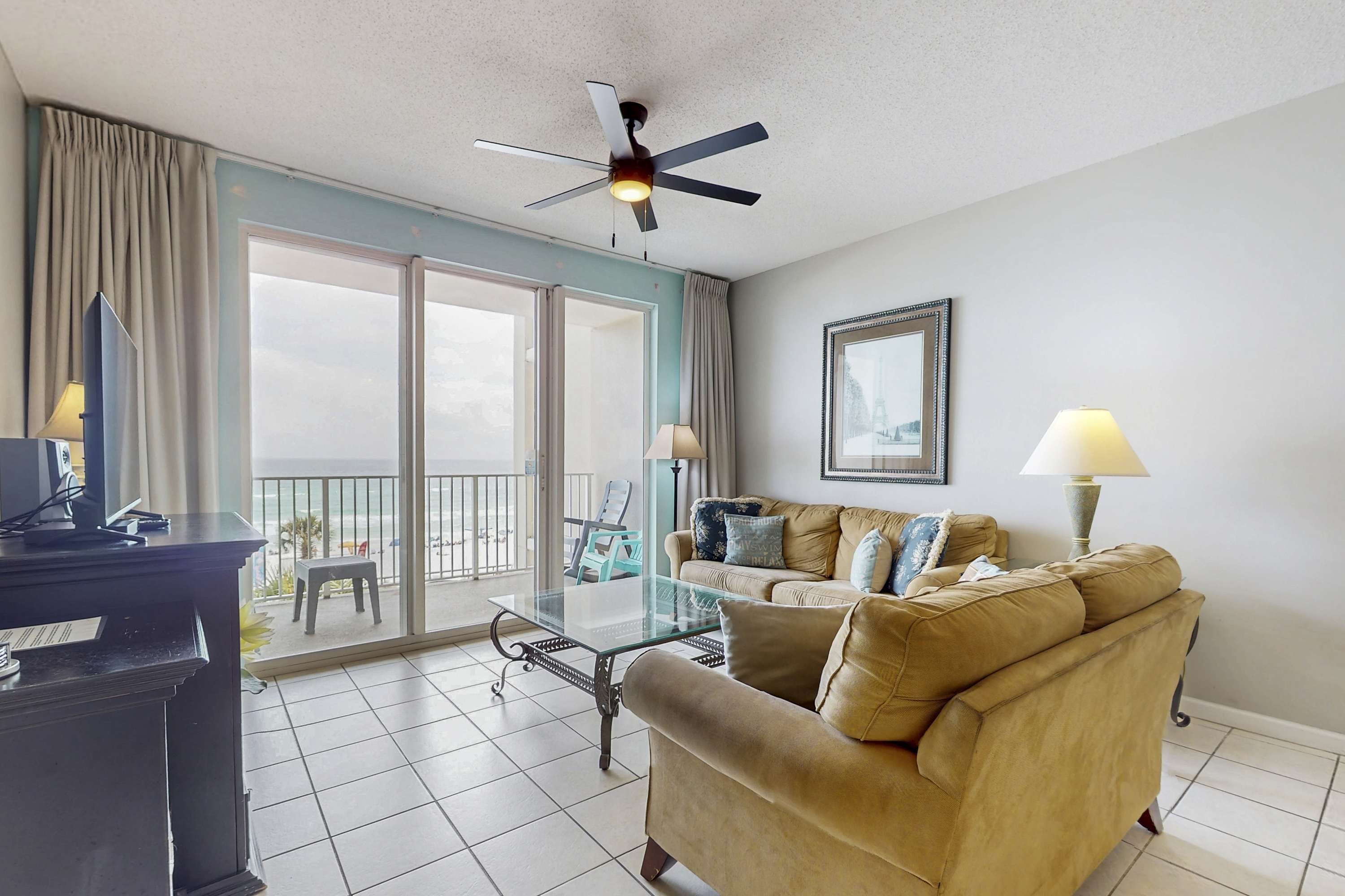 A living room with a glass coffee table, beige sofa, and a ceiling fan.