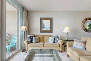 A living room with a beige sofa, a glass coffee table, and a view of the Eiffel Tower through a window. - Majestic Sun B305 | Beachfront Bliss! (Miramar Beach)