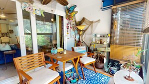 Un espace patio accueillant, agrémenté de meubles en bois, d’un tapis à motifs et d’objets décoratifs, notamment une sculpture de papillon et une lampe.