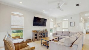 A spacious living room with a large flat-screen TV, a sofa, a wooden coffee table, and a wicker chair. - Gorgeous coastal home with plenty of space with shared pool & beach access (Miramar Beach)