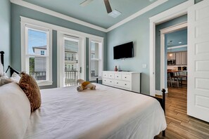 Ein Schlafzimmer mit einem großen Bett, einem flachbildfernseher an der Wand und Blick auf die Küche durch eine offene Tür.