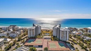 Área residencial costeira com vários edifícios altos, quadras de tênis e vista clara para o oceano.
